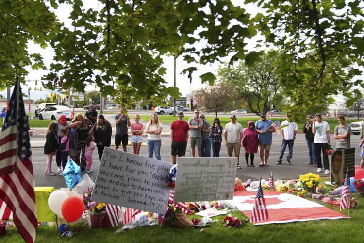 Mourners gather at a public vigil holding flags and a scripture sign, reflecting the national response tied to the Charlie Kirk post firing settlement.